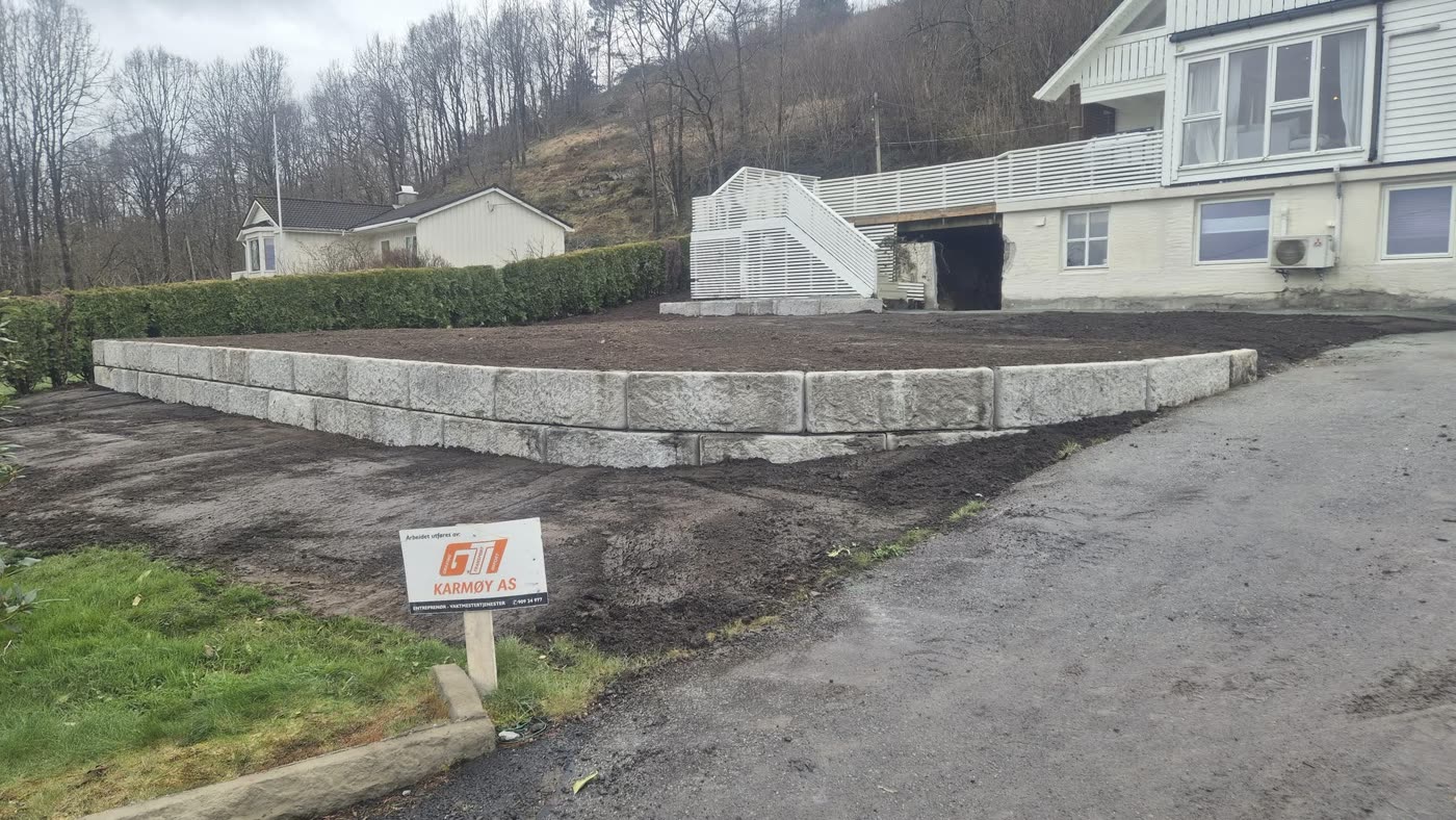 Ny steinmur og planert hage ved et hvitt hus